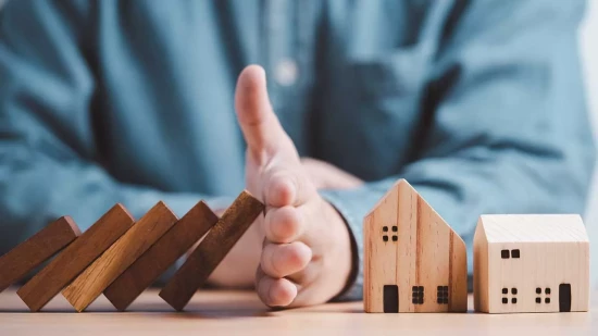hand blocking wooden blocks from falling over onto a toy wooden home